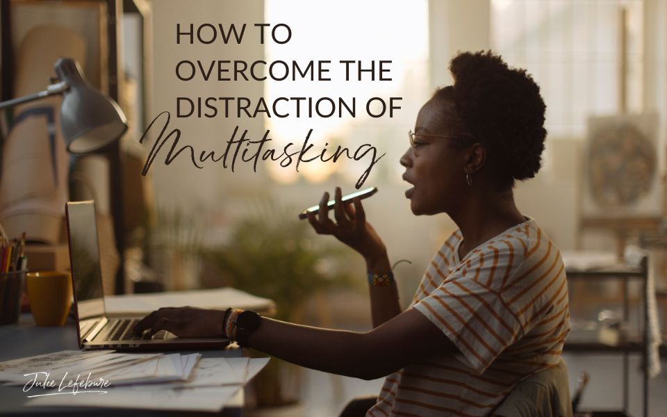 How to Overcome the Distraction of Multitasking | woman sitting at desk, one hand on laptop keyboard, the other hand holding her phone while she's speaking into it